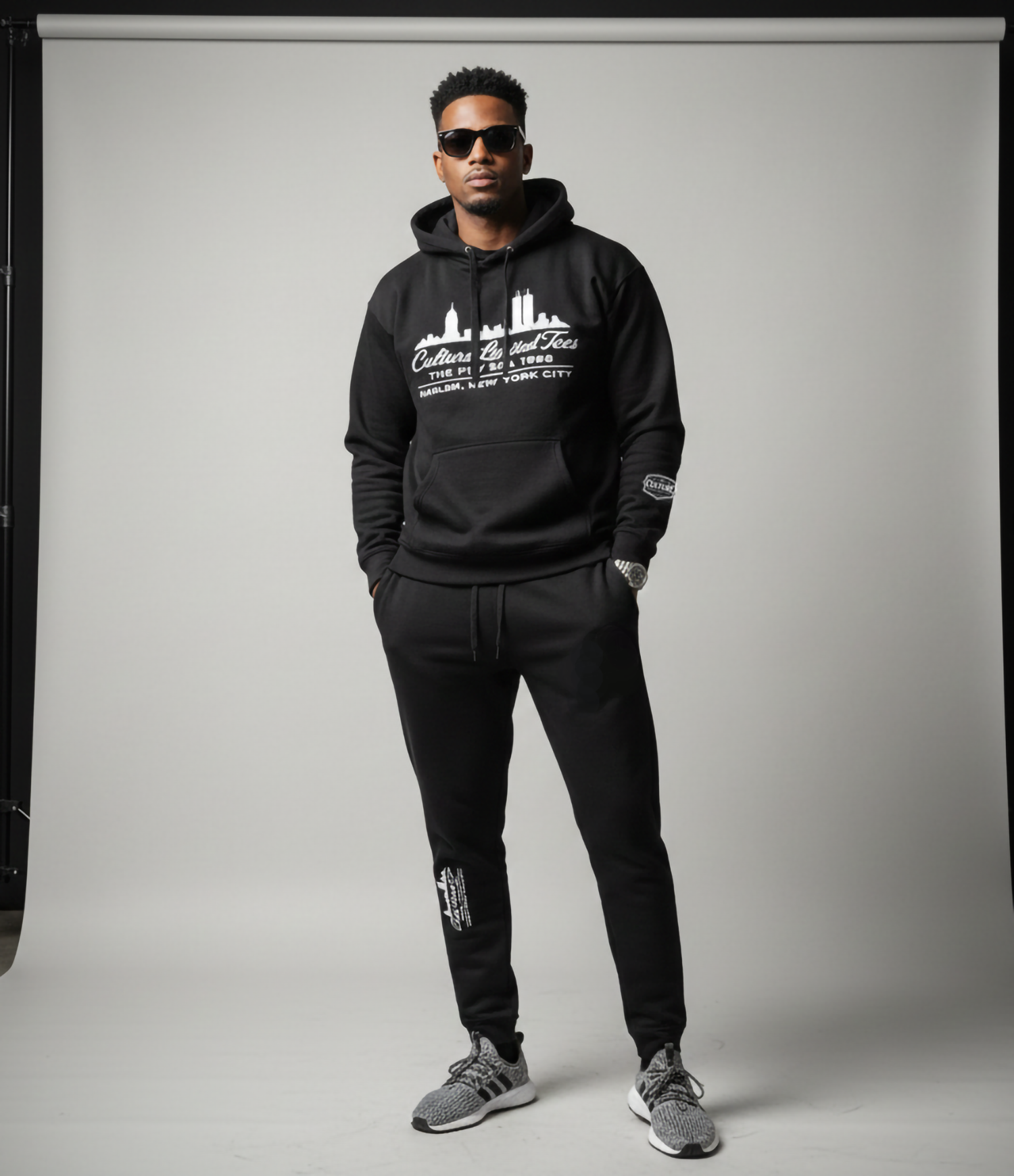 Man wearing a black hoodie with white text and graphics, standing against a plain background